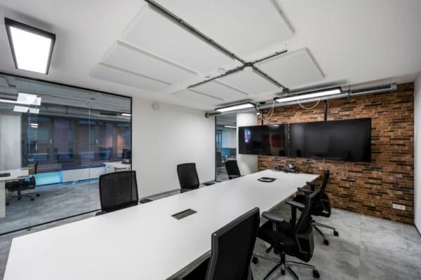 Moderne vergaderruimte aan de Harry Banninkstraat met lange witte tafel, zwarte stoelen en twee grote schermen aan een bakstenen muur.